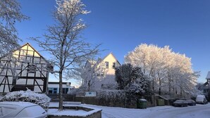 A snow-covered street with houses, a car, and a bench. - Engemann Modern Retreat (Kassel)