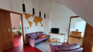 A modern living room with a world map wall, a sofa, a coffee table, and a TV. - Engemann Modern Retreat (Kassel)