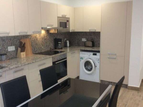 A compact kitchen with a microwave, oven, and washing machine.