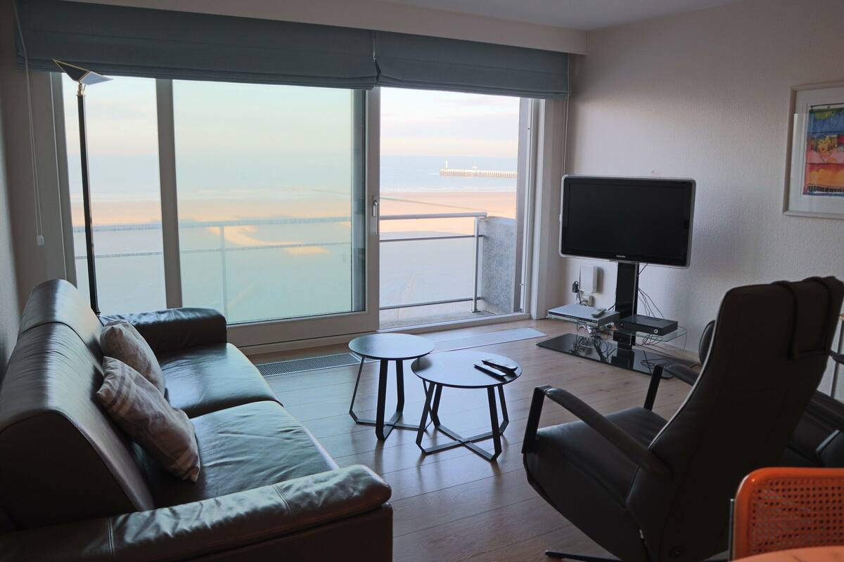 A modern living room with a large window, a sofa, a coffee table, a TV, and a chair.
