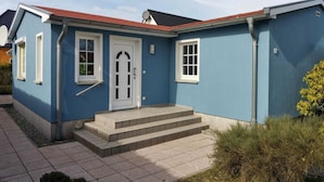 Ein eingeschossiges Haus mit rotem Dach, einer weißen Tür und einer kleinen Treppe zum Eingang.