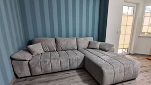 Ein graues Ecksofa mit Chaiselongue, platziert vor einer blau gestreiften Wand in einem Raum mit Holzboden.