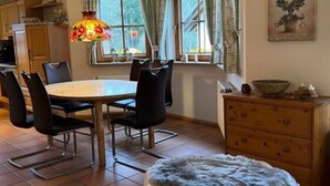 Un comedor con mesa y sillas de madera, una lámpara colgante con motivos florales, una ventana con cortinas y un reloj en la pared.