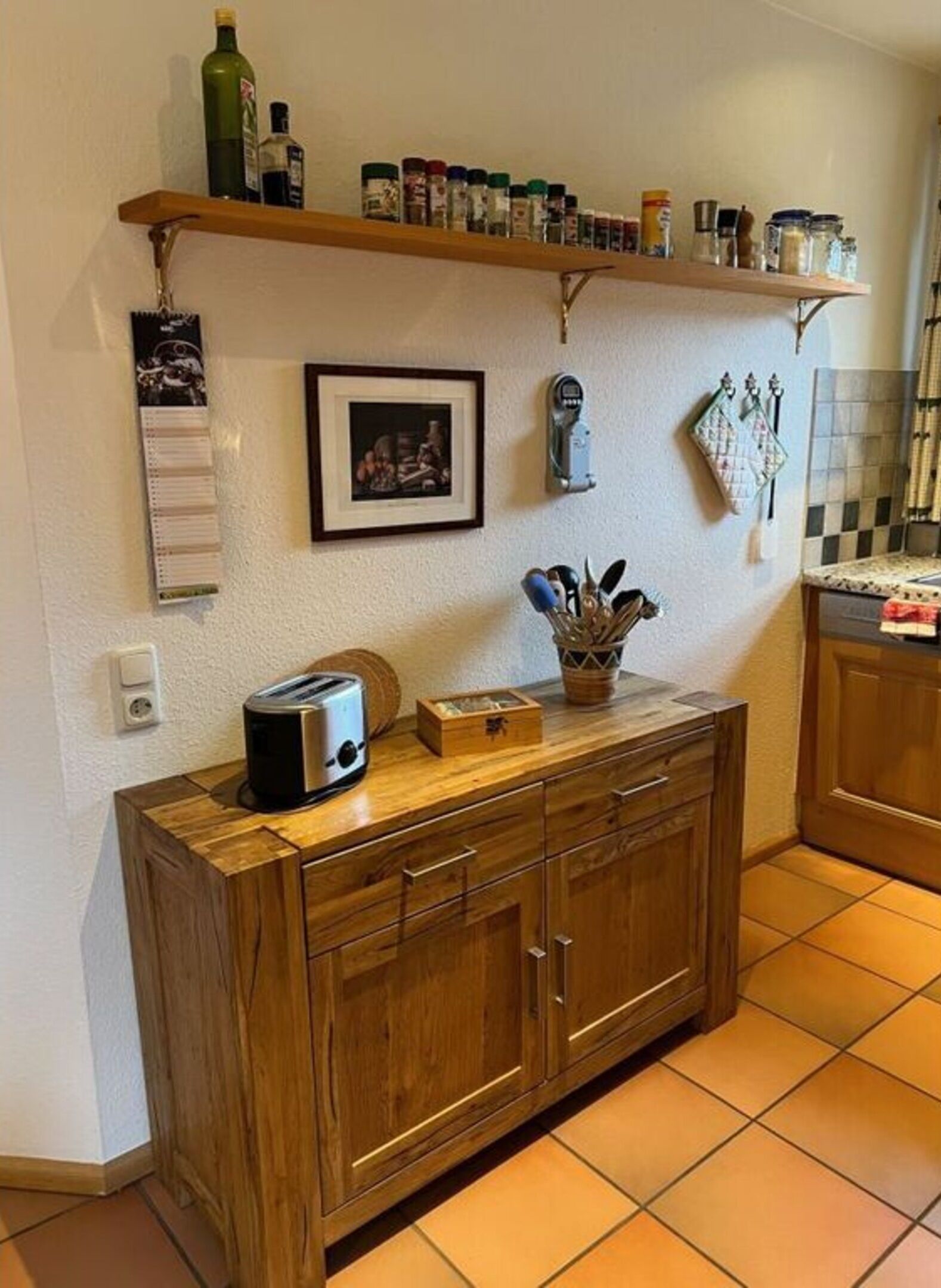 A kitchen with wooden cabinets, a toaster, a spice rack, and a framed picture on the wall.