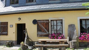 Un bâtiment rustique à la façade jaune, avec des volets en bois et un banc en bois devant.