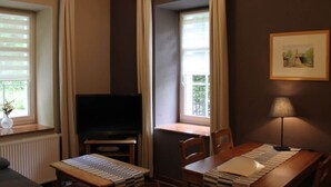 Une pièce avec une télévision, une table avec des chaises, une fenêtre avec des rideaux et une lampe.