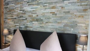Une chambre avec un lit adossé à un mur en pierre, deux lampes de chevet et une tête de lit noire.