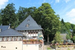 A traditional half-timbered building with a balcony, surrounded by lush greenery and trees. - Holiday Apartment Comfortable Vacation Home (Annaberg-Buchholz)