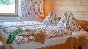 A room with a wooden wall, a window with curtains, a bed with patterned bedding, and a lamp. - Chalet in Filzmoos Near Tauern Mountains (Filzmoos)