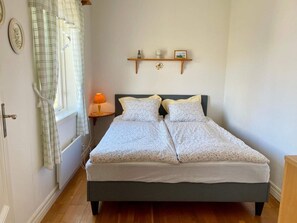 A bedroom with a bed, a bedside table with a lamp, a shelf with decorative items, and a window with curtains. - 5 Person Holiday Home in Lottorp (Löttorp)