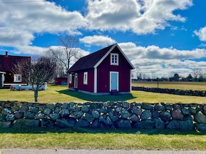 A red house with a stone wall in front, a clear blue sky, and a grassy field.