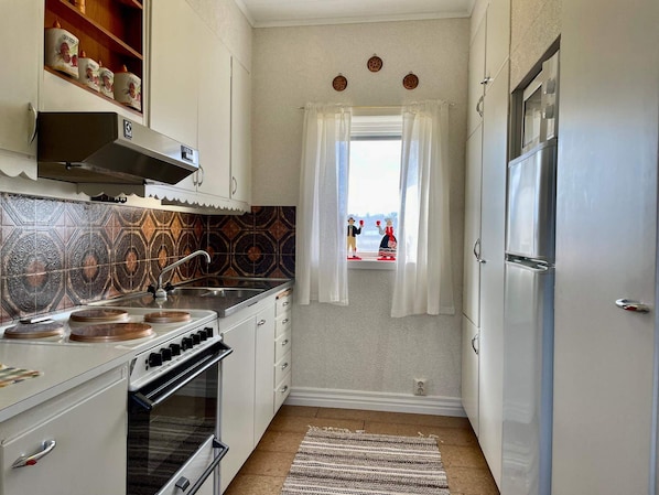 A compact kitchen with white cabinets, a stove, oven, and a window with curtains.