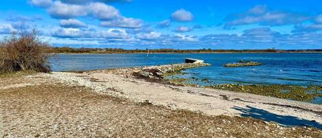 A coastal landscape with a sandy beach, rocky outcrops, and a clear blue sky.