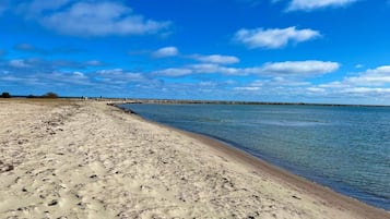 Uma praia arenosa, mar calmo e céu claro.