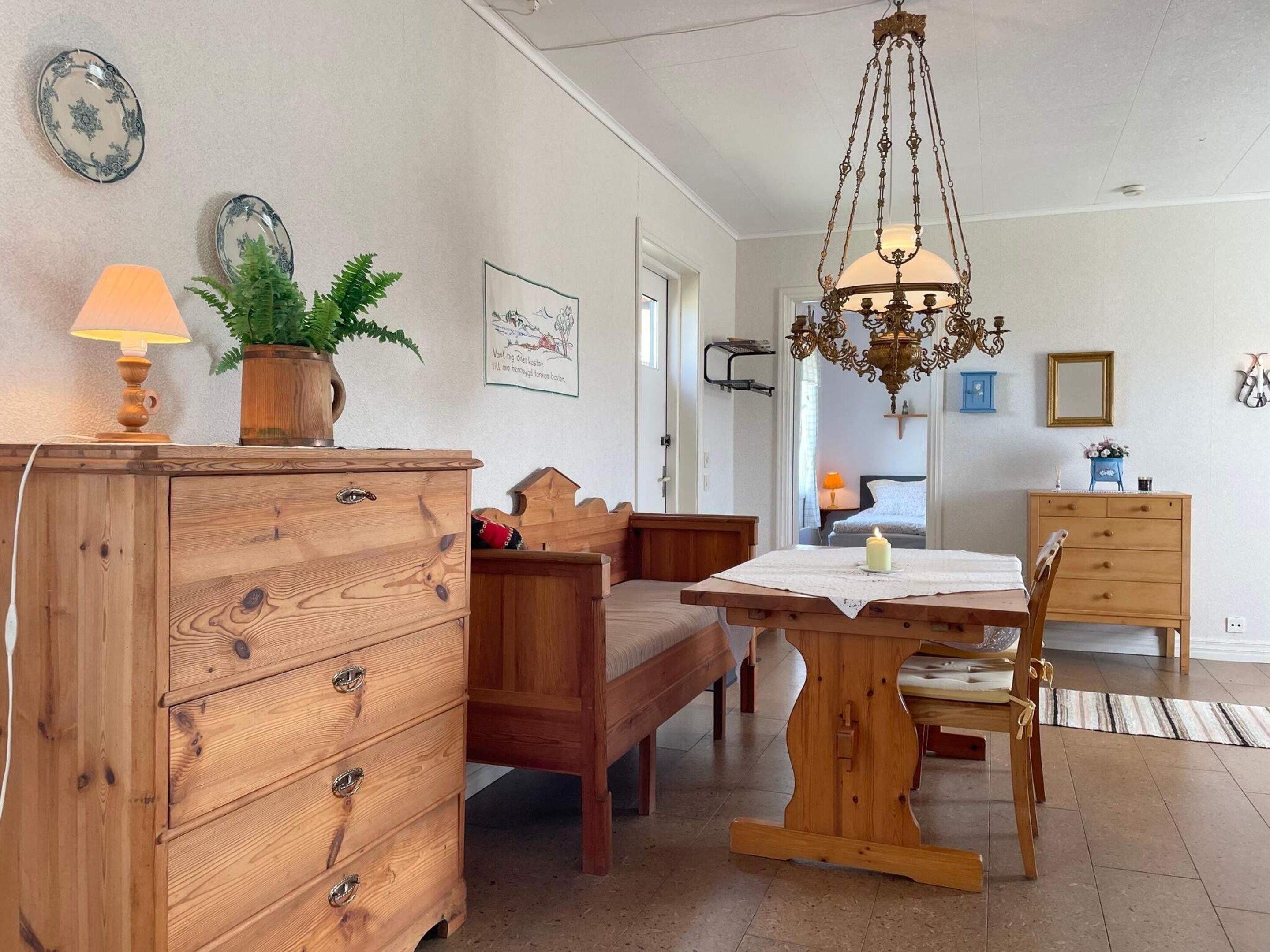 A cozy room with a wooden dresser, a bench, a table with a candle, and a chandelier.