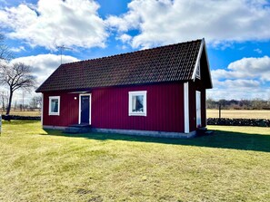 Ein rotes Holzhaus mit dunklem Dach, weißer Verzierung und einer kleinen Veranda.