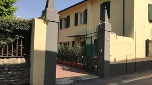 Un bâtiment doté d’une entrée fermée par un portail, d’un mur en pierre et d’une zone pavée agrémentée de plantes en pot.