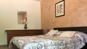 Une chambre à coucher comprenant un lit, une commode, un miroir et une illustration botanique encadrée accrochée au mur.
