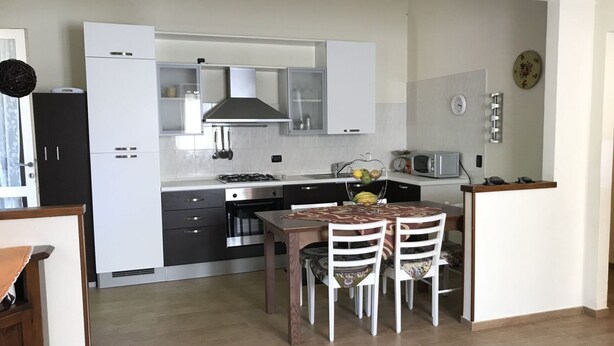 Une cuisine moderne avec des meubles blancs, une cuisinière à gaz, un four à micro-ondes et un coin repas comprenant une table et des chaises.