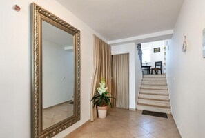 Un pasillo con un espejo grande y ornamentado, una planta en maceta y una escalera que lleva a otra habitación.