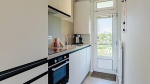 A compact kitchen with a built-in oven, a coffee maker, and a door leading to a balcony. - Coastal Escape w/ Sauna (Zoutelande)