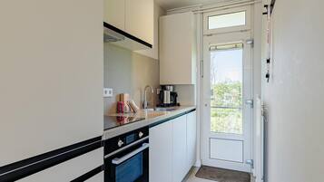 A compact kitchen with a built-in oven, a coffee maker, and a door leading to a balcony.