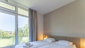 A hotel room with a large window, a bed with white linens, and a nightstand with a lamp. - Coastal Escape w/ Sauna (Zoutelande)