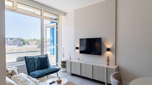 A modern living room with a sofa, armchair, coffee table, and a TV mounted on the wall. - Coastal Escape w/ Sauna (Zoutelande)