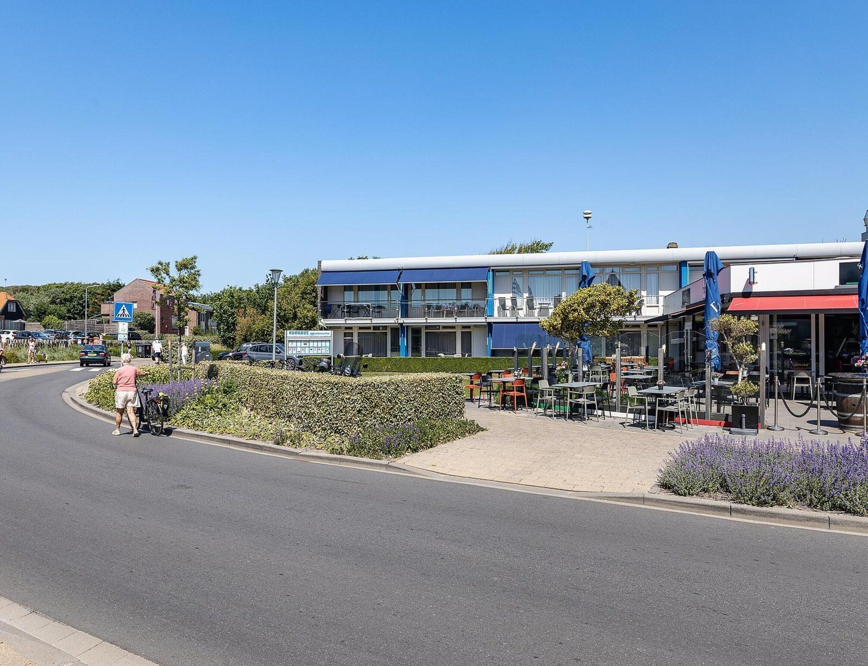 A building with a blue and white facade, outdoor seating area, and a pedestrian pathway.