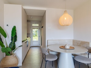 Uma cozinha moderna com armários brancos, uma área de jantar com mesa e cadeiras redondas, e um lustre.
