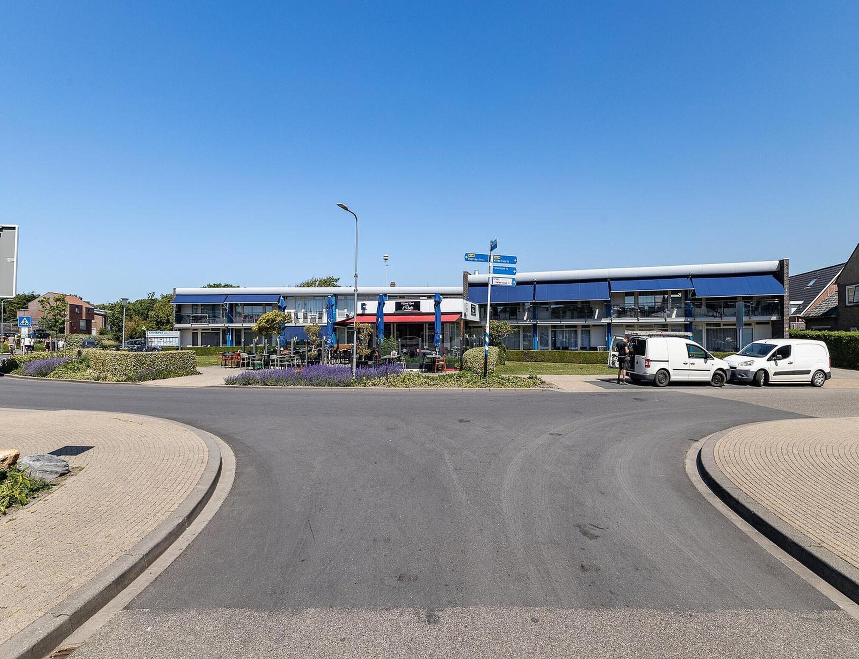 Ein Gewerbegebiet mit Kreisverkehr, einem Restaurant mit Außenbereich und einem Parkplatz mit weißen Lieferwagen.