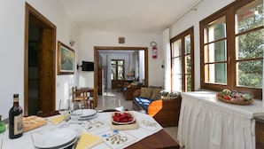 A dining area with a table set for four, a sofa, and a window with a view of greenery. - Apartment in Sassetta With Pool and Garden (Castagneto Carducci)