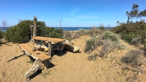 A rustic wooden bench and table set in a sandy area with sparse vegetation and a clear view of the ocean. - Apartment in Sassetta With Pool and Garden (Castagneto Carducci)