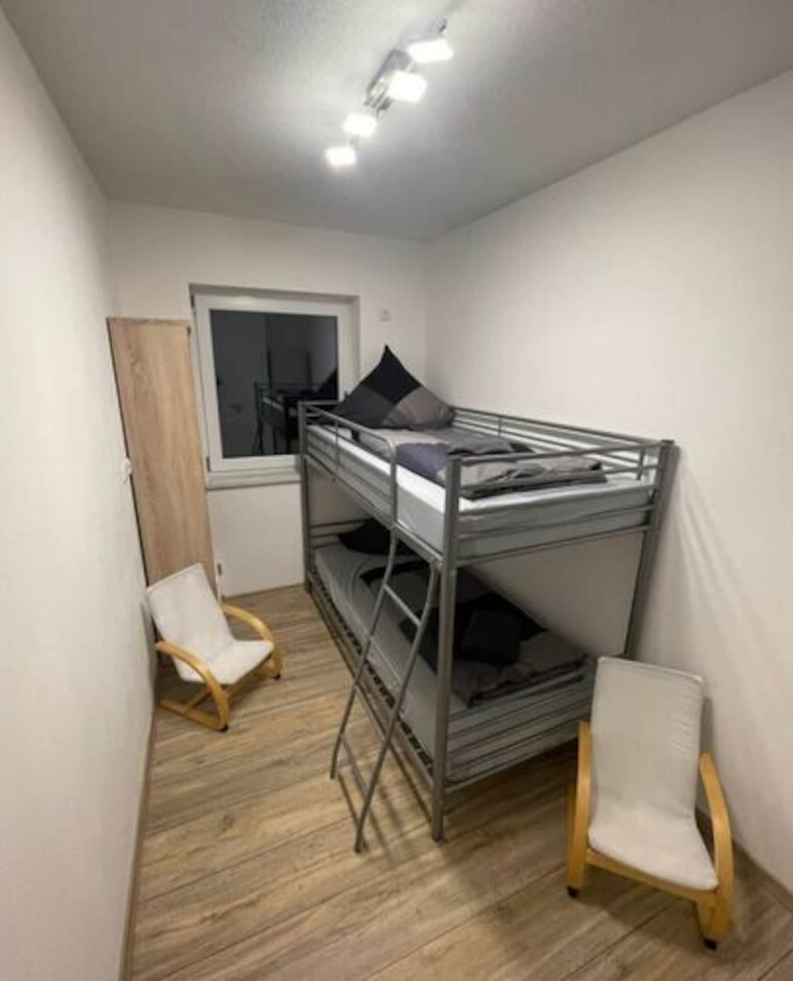 A small, compact room with a bunk bed, a wooden chair, and a desk.