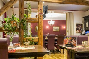 A restaurant with wooden beams, red walls, and a chandelier. Tables are set with menus and a sign for 'Wurstinger'. - Holiday Apartment in Klein Upahl (Klein Upahl)