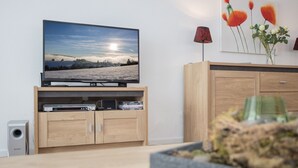 Olohuoneessa on litteänäyttöinen televisio, joka on sijoitettu puiseen jalustaan, kaiutin ja kaappi, jossa on erilaisia viihdelaitteita.