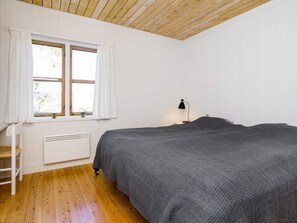 A bedroom with a bed, a nightstand, a lamp, a window with curtains, and a radiator.