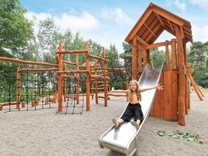 Une aire de jeux avec un toboggan, des structures d’escalade et une cabane en bois.