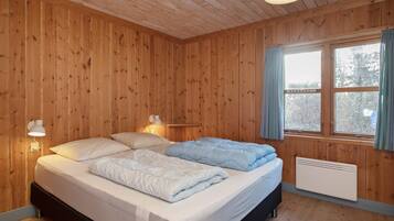 A wooden-paneled room with a bed, two bedside lamps, a window with curtains, and a radiator.