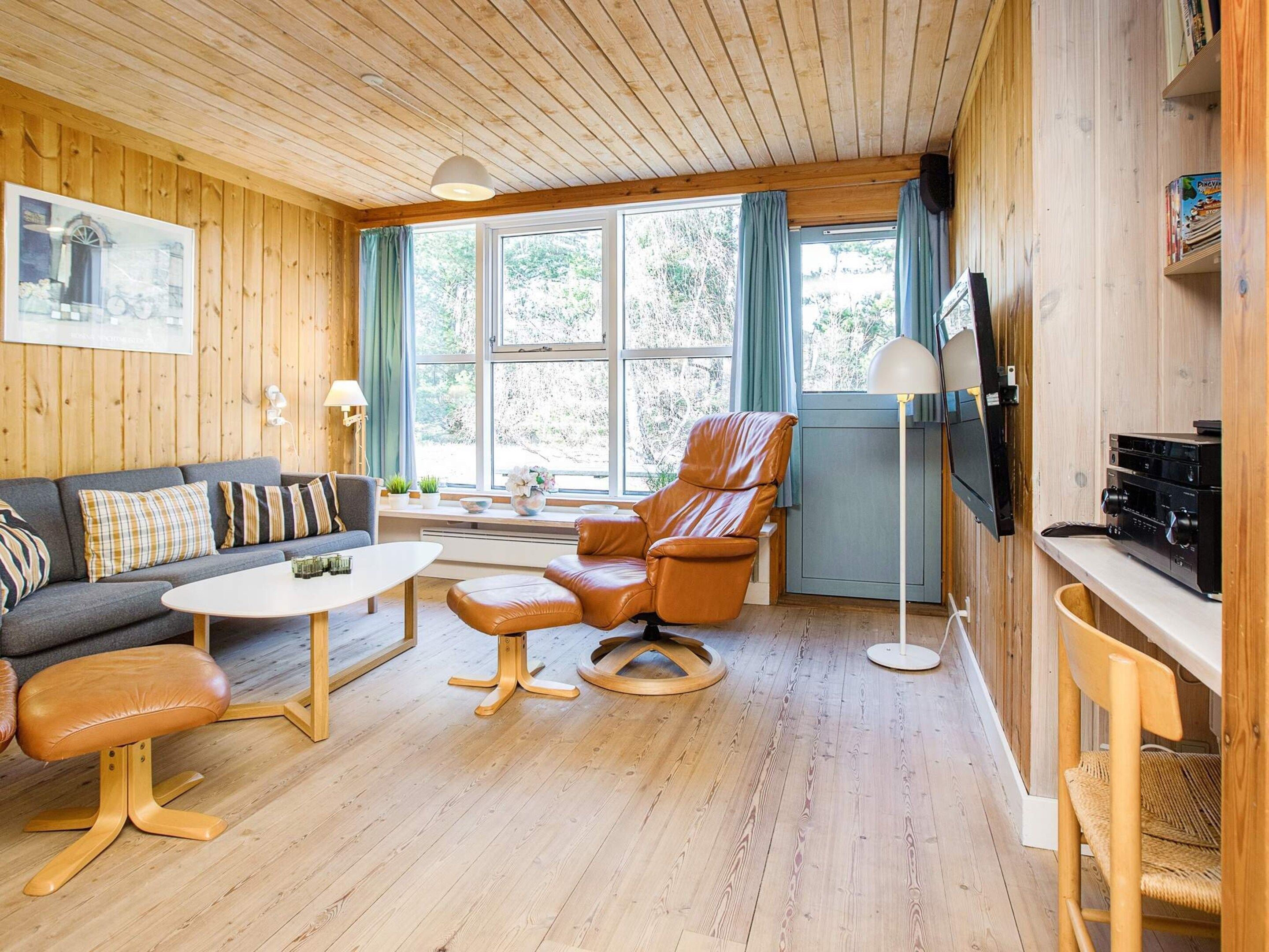 A cozy living room with wooden walls, a sofa, a leather armchair, a coffee table, and a TV.
