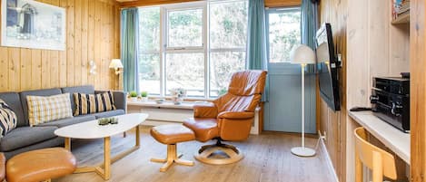 A cozy living room with wooden walls, a sofa, a leather armchair, a coffee table, and a TV.