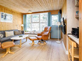 Una sala de estar acogedora con paredes de madera, un sofá, un sillón de cuero, una mesa de centro y un televisor.