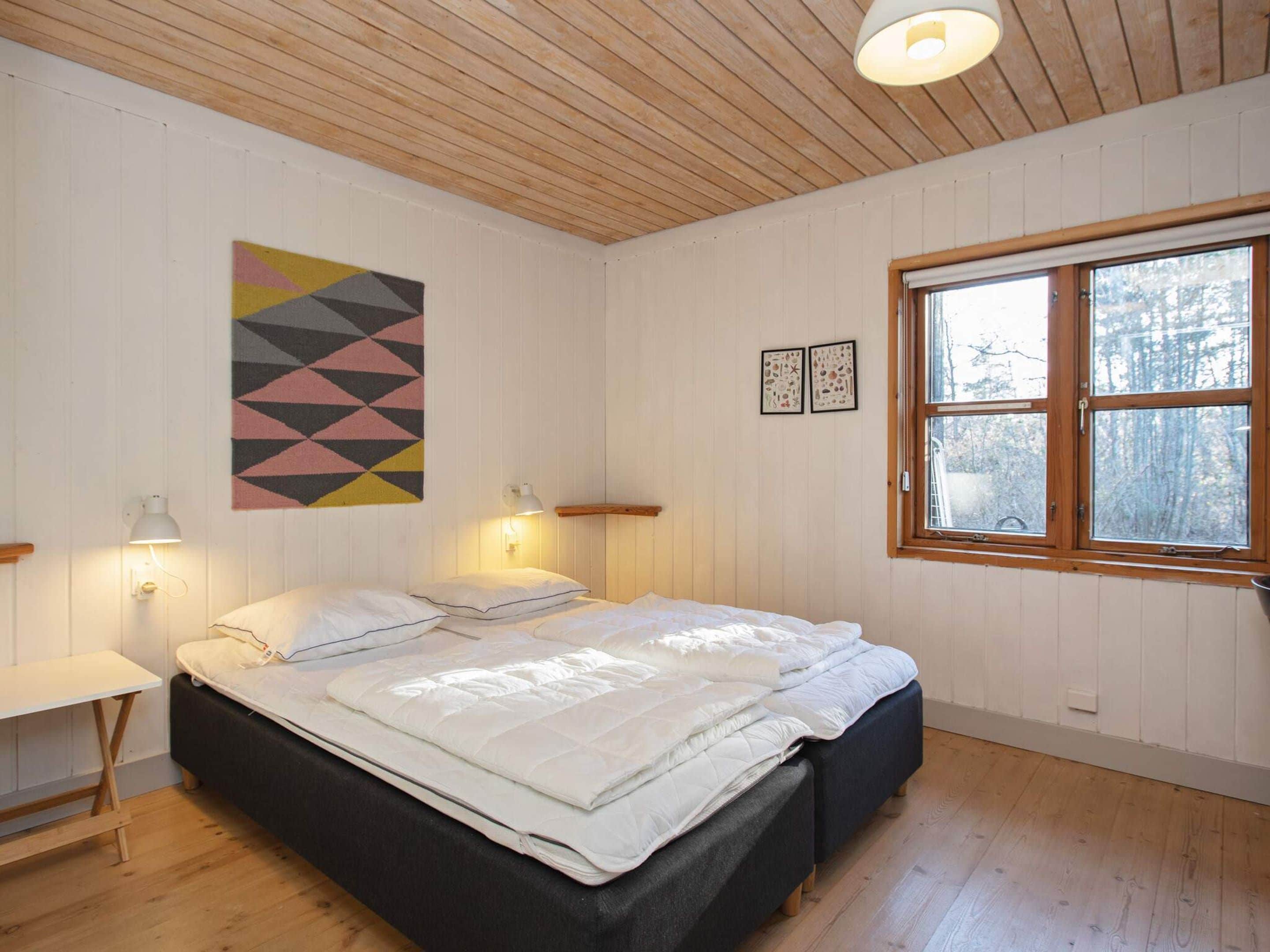A bedroom with a bed, bedside lamps, a window, and a geometric wall hanging.