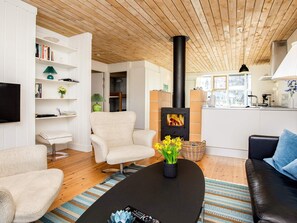Un salon moderne doté d’une cheminée, de sièges confortables et d’un coin cuisine visible à travers une porte ouverte.