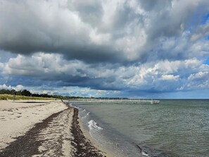 Una playa con arena, un muelle que se adentra en el agua y un cielo nublado.