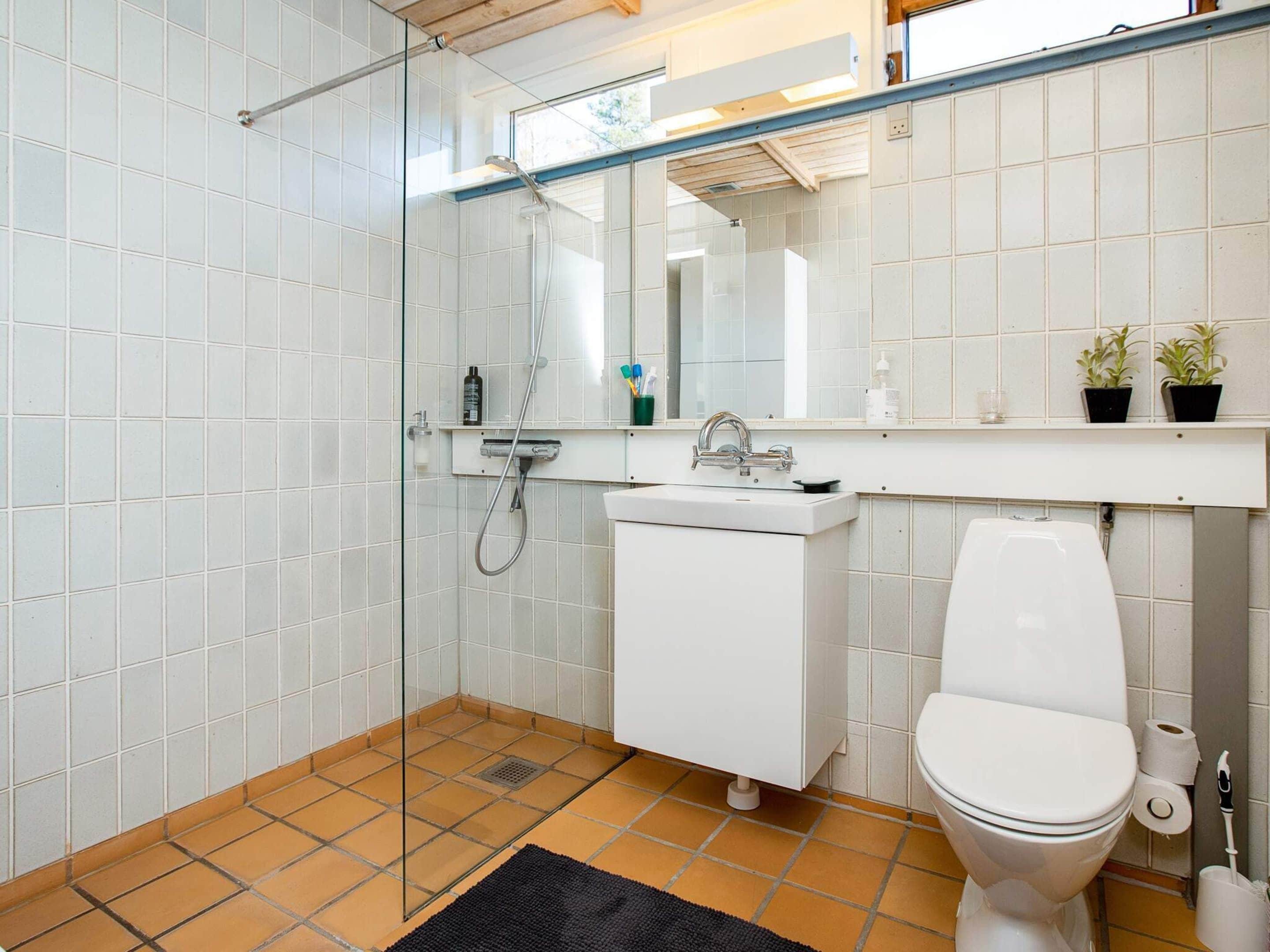 A modern bathroom with white tiles, a glass shower enclosure, a white sink, and a toilet.