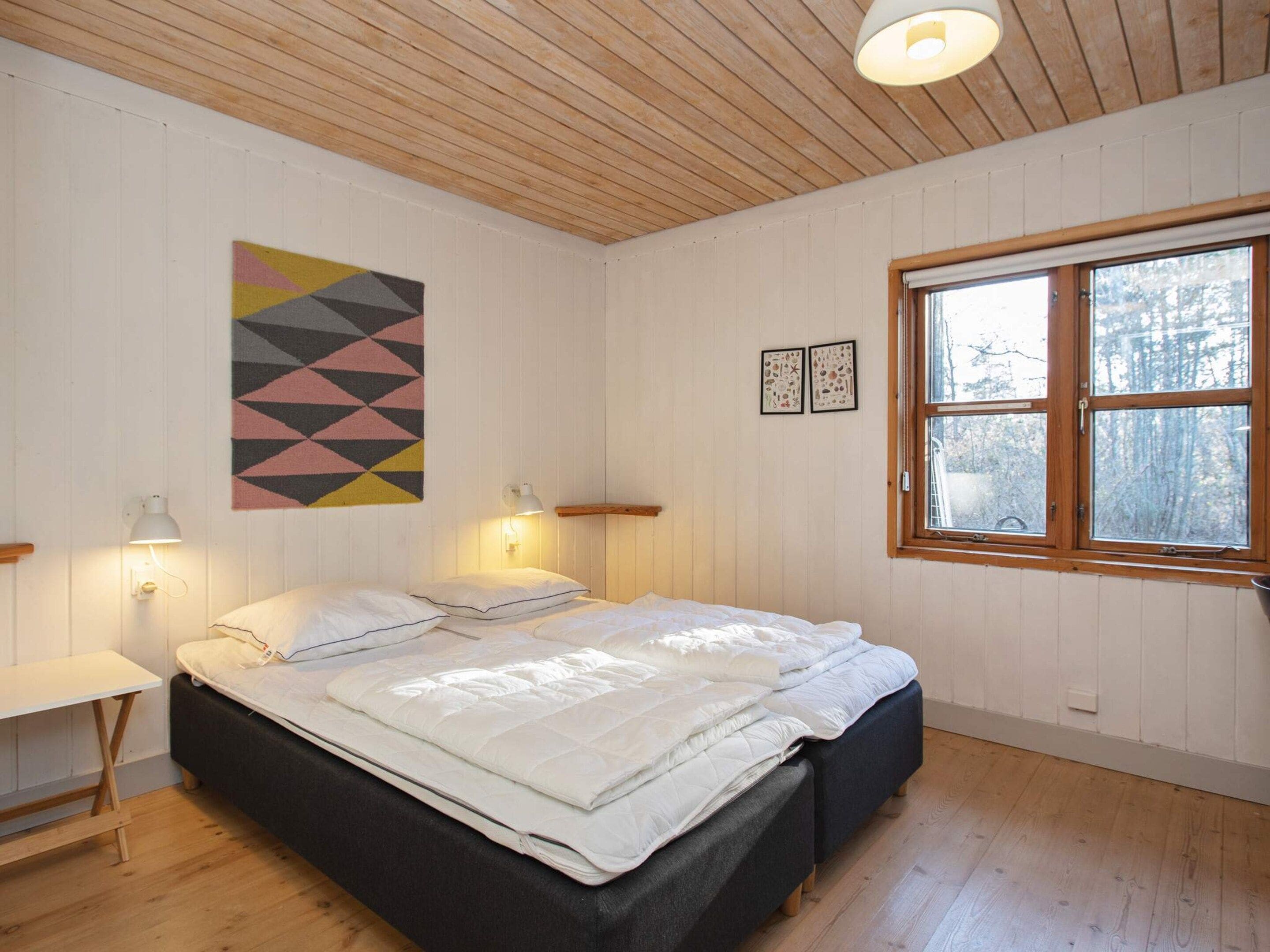 Ein Schlafzimmer mit einem Bett, Nachttischlampen, einem Fenster und einem Wandbehang mit geometrischem Muster.
