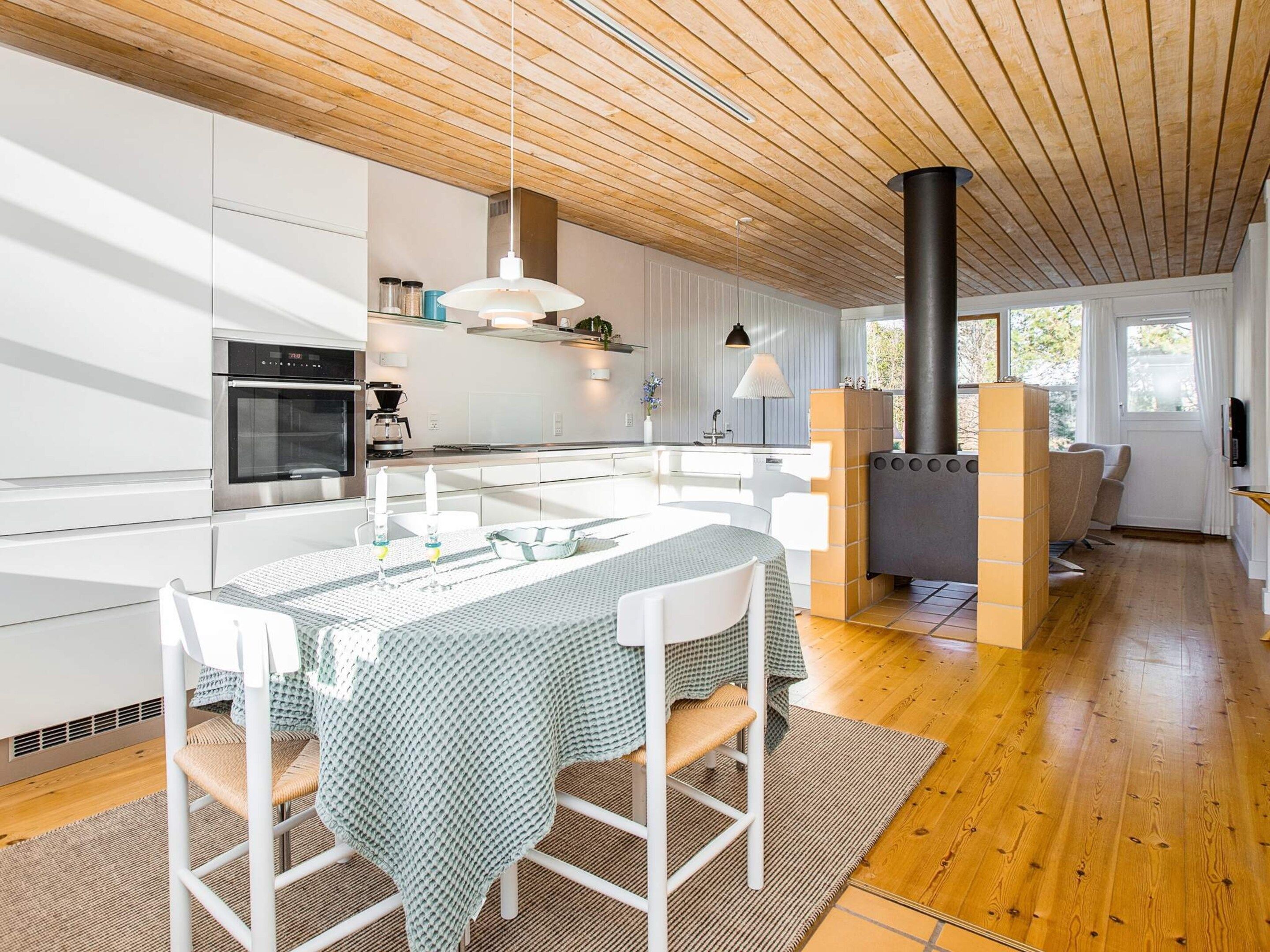 A modern kitchen with white cabinetry, a central island with seating, a built-in stove, and a dining area with a table and chairs.