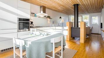 A modern kitchen with white cabinetry, a central island with seating, a built-in stove, and a dining area with a table and chairs.
