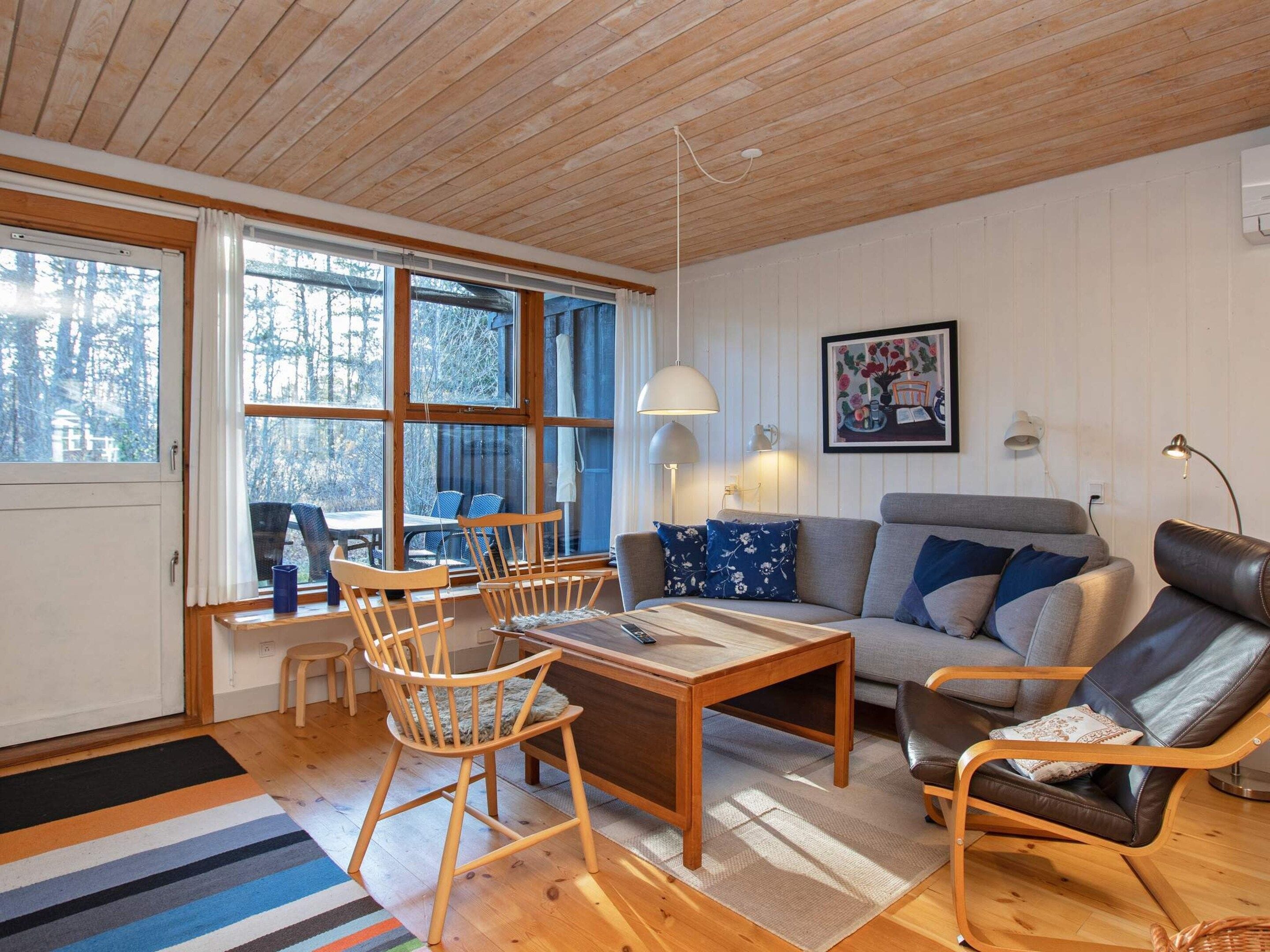 Un salon chaleureux avec un plafond en bois, un canapé, une table basse et un coin repas comprenant des chaises et une table.